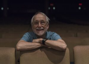 Erica Hong/Courier Theatre instructor and director, Whitney Rydbeck sits alone in the audience seating of Sexson Auditorium on Wednesday, July 08, 2015 at PCC. Rydbeck has retired after four decades at PCC but cheerfully returned to be photographed on the other side of the stage, as posters of his final directorial performance, Spoon River still hang on the walls.