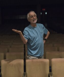 Erica Hong/Courier Theatre instructor and director, Whitney Rydbeck stands alone in the audience seating of Sexson Auditorium on Wednesday, July 08, 2015 at PCC. Rydbeck has retired after four decades at PCC but cheerfully returned to be photographed on the other side of the stage, as posters of his final directorial performance, Spoon River still hang on the walls.